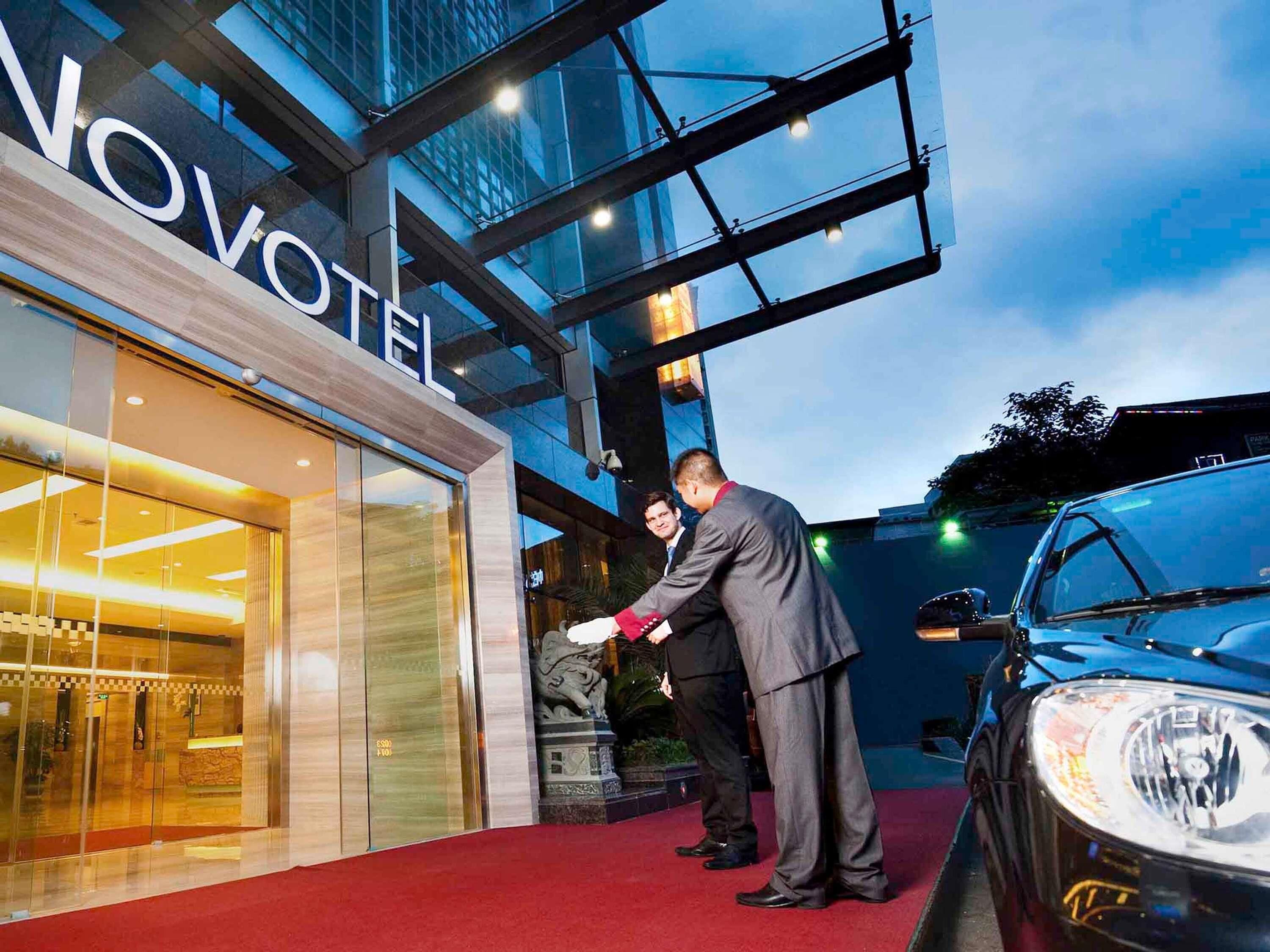A hotel entrance with a glass facade, a red carpet, and a statue outside.