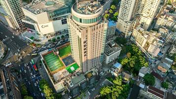 A high-rise building with a rooftop terrace, surrounded by other buildings and a green space.