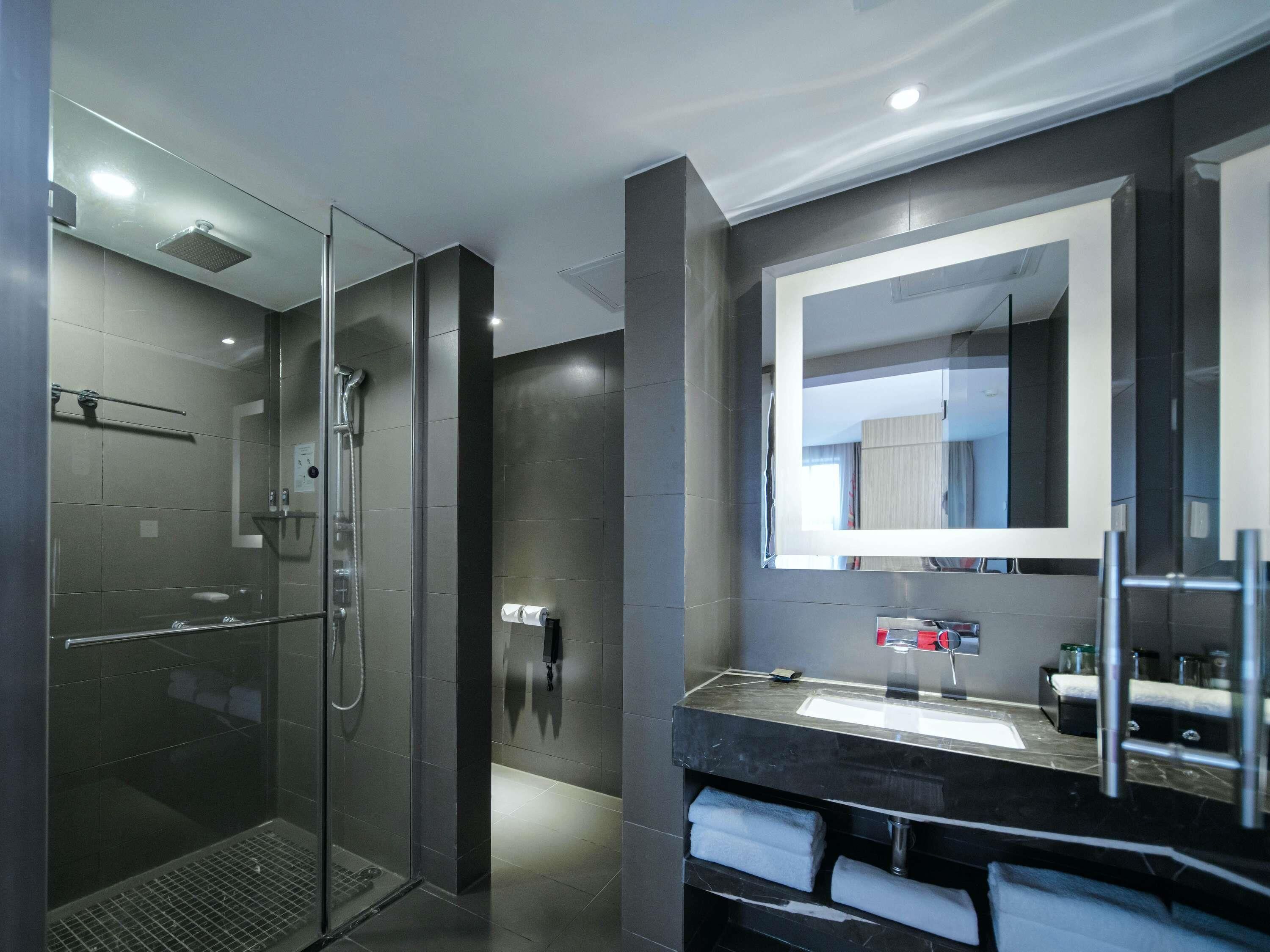 A modern bathroom with a glass-enclosed shower, a large mirror, and a black countertop with a sink.