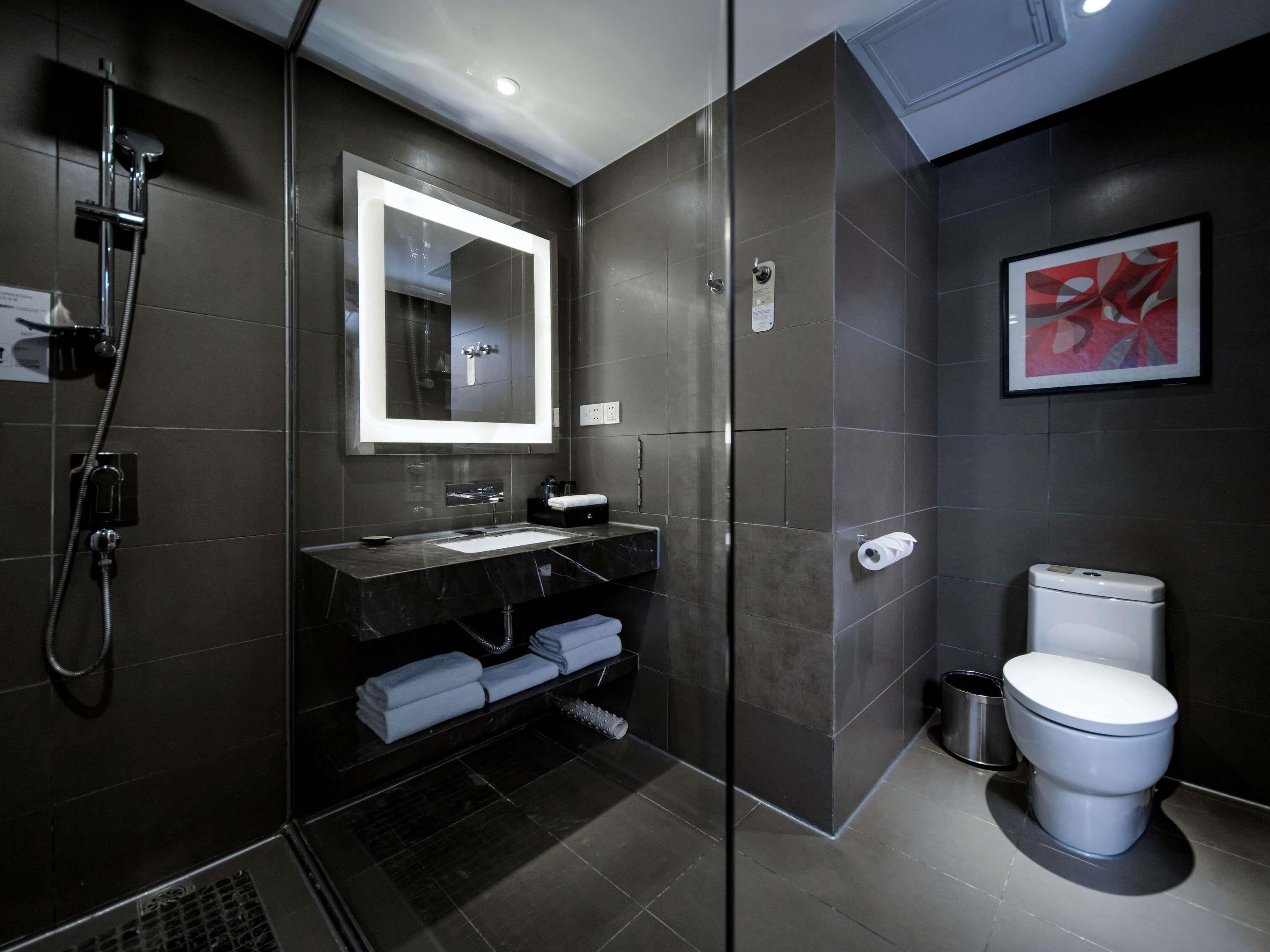 Une salle de bain moderne avec une douche à parois de verre, un grand miroir, des toilettes blanches et un tableau abstrait encadré accroché au mur.