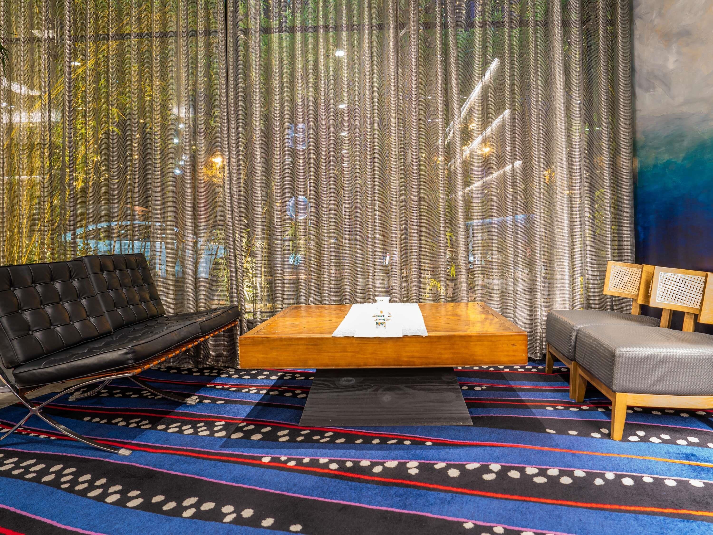 A room with a black leather sofa, a wooden bench, and a patterned carpet.