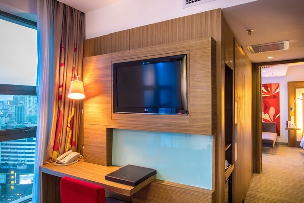Habitación de hotel con televisión de pantalla plana montada en la pared, un escritorio con teléfono y una silla roja.