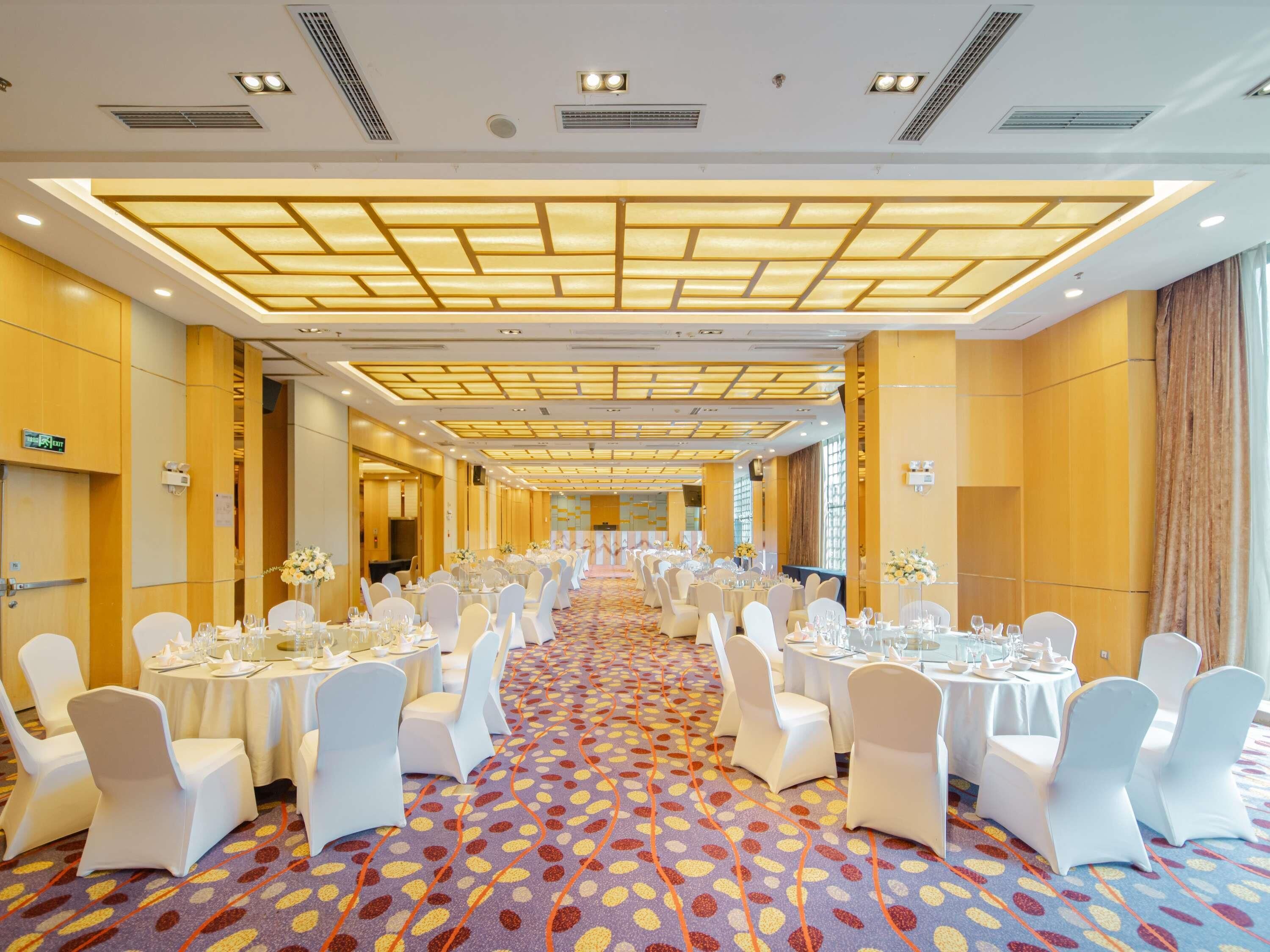Ein Hotelkonferenzraum mit runden Tischen, weißen Stühlen und einem gemusterten Teppich.