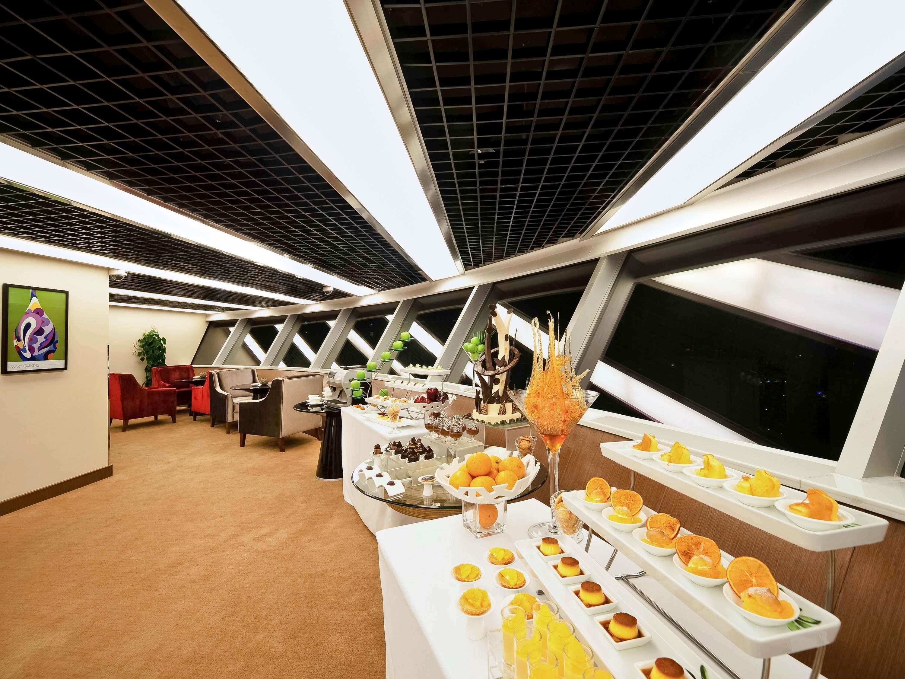 A modern room with a high ceiling, a large window, and a buffet table with various food items.