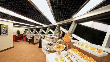 A modern room with a high ceiling, a large window, and a buffet table with various food items.