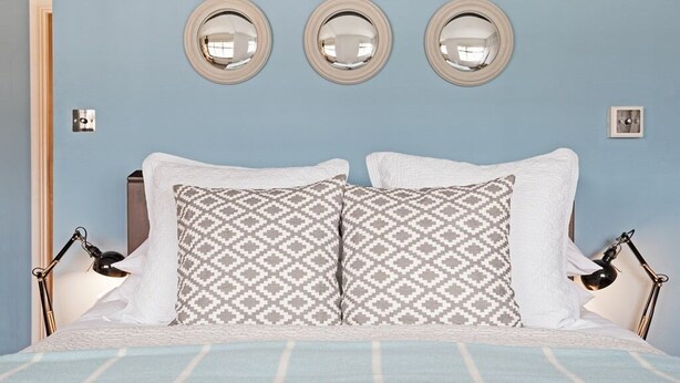 A bed with patterned pillows, a blue-striped blanket, and three wall-mounted mirrors. - The George & Dragon (Devizes)