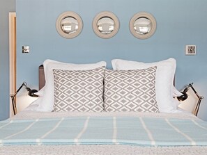 A bed with patterned pillows, a blue-striped blanket, and three wall-mounted mirrors.