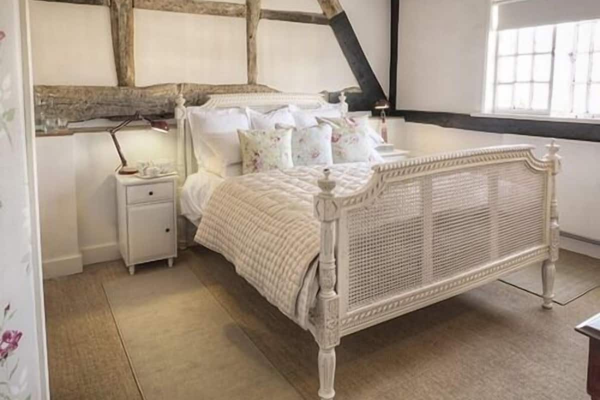 Un dormitorio con una cama con dosel blanco, una mesita de noche y una ventana con persianas.