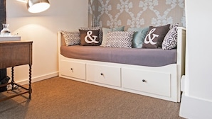 A cozy room with a sofa bed, patterned cushions, a desk, and a lamp. - The George & Dragon (Devizes)