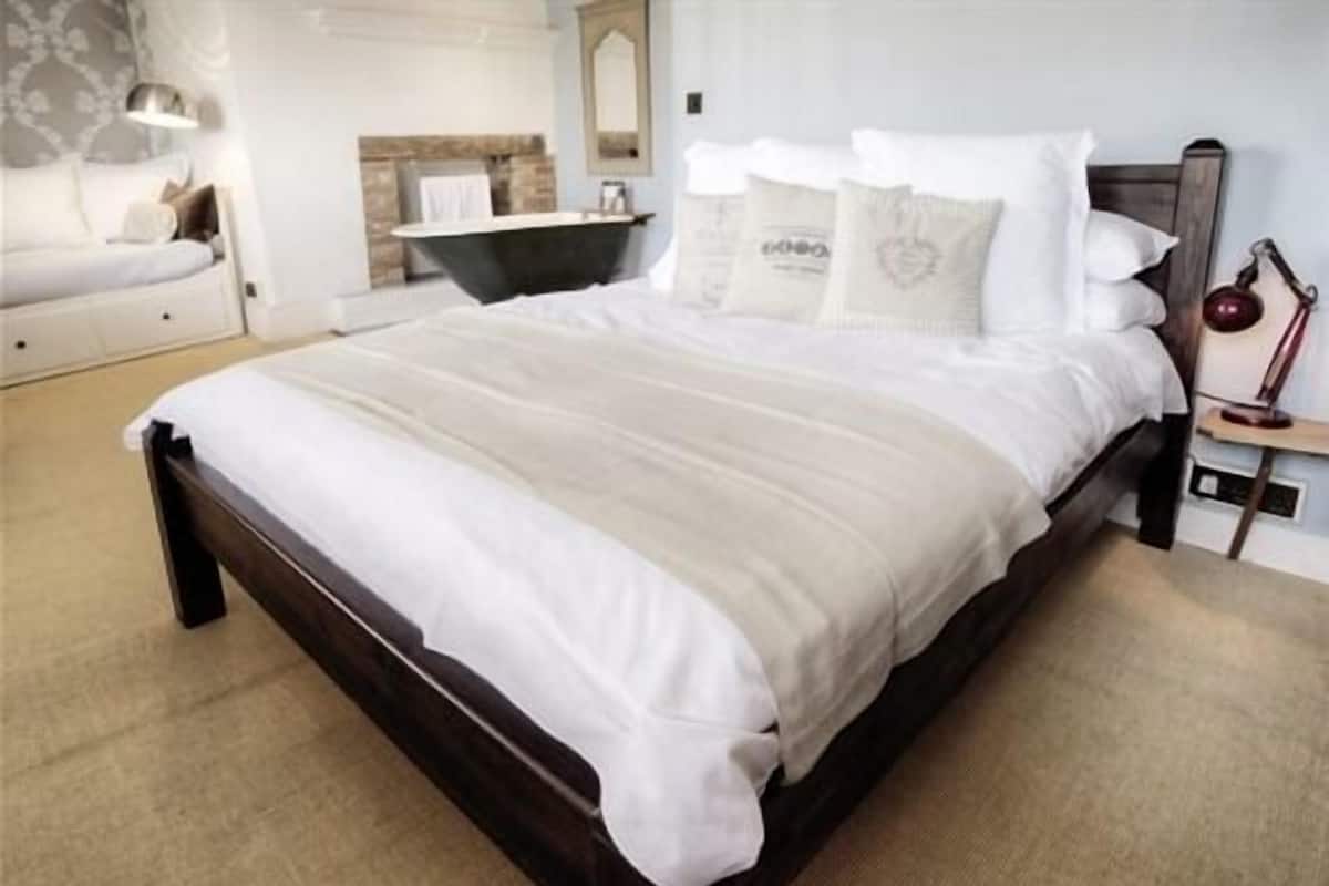 Un dormitorio con una cama de madera oscura, ropa de cama blanca, una mesita de noche con lámpara y un espejo en la pared.