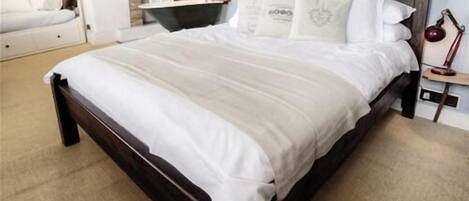 A bedroom with a dark wooden bed, white bedding, a bedside table with a lamp, and a mirror on the wall.