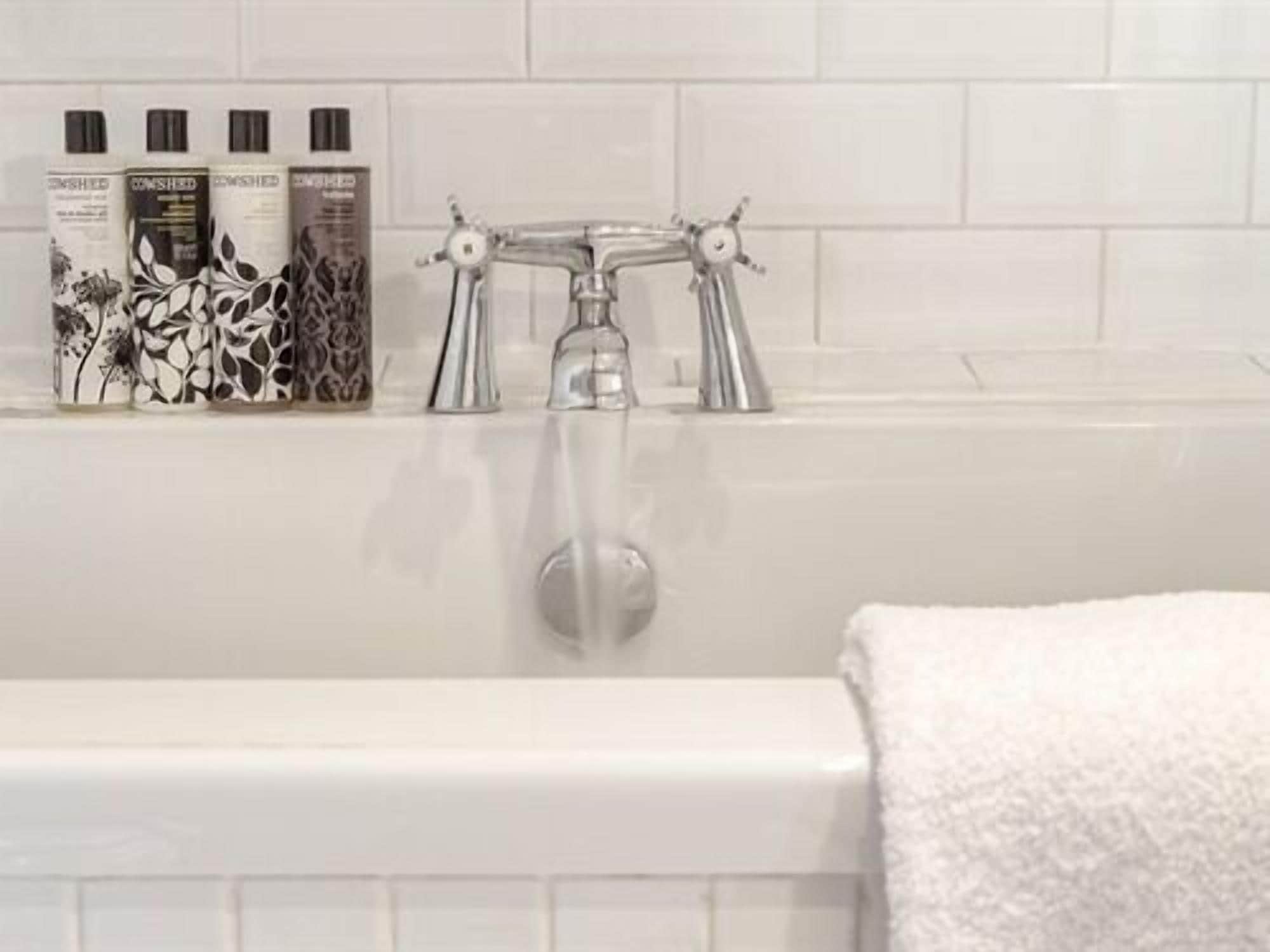 Une salle de bain avec une baignoire blanche, un robinet argenté et une étagère murale où sont rangés les produits de toilette.