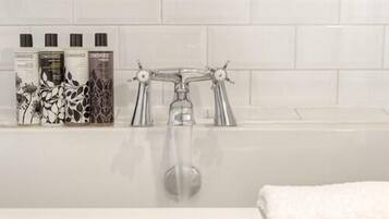 Une salle de bain avec une baignoire blanche, un robinet argenté et une étagère murale où sont rangés les produits de toilette.