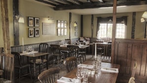 A restaurant with wooden tables and chairs, framed pictures on the walls, and a window with curtains. - The George & Dragon (Devizes)
