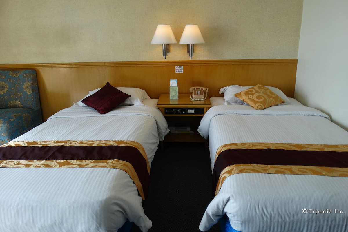A hotel room with two single beds, a nightstand with a lamp, a telephone, and a sign prohibiting smoking.