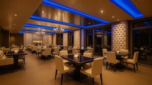 A spacious dining area with multiple tables and chairs, a chandelier, and a modern ceiling design with blue lighting accents. - Almondz Hotel (New Delhi)