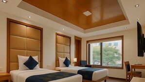 A hotel room with two beds, a desk, and a chair. - Almondz Hotel (New Delhi)