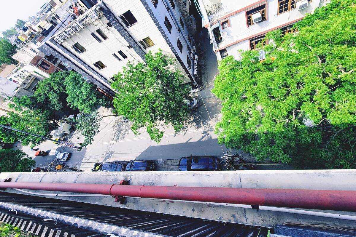 A multi-story building with balconies and windows, a street with parked cars, and a red pipe running along the sidewalk.