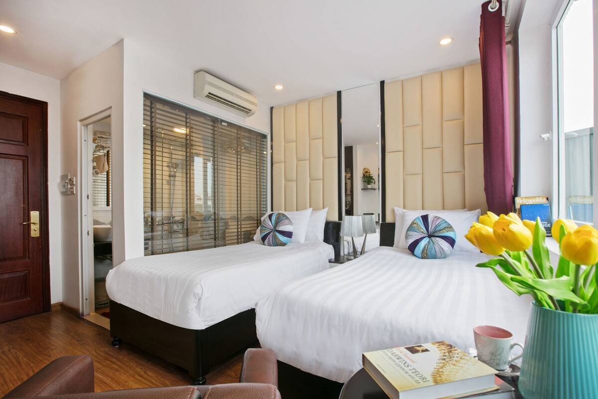 A hotel room with two beds, a large mirror, an air conditioning unit, and a window with curtains.