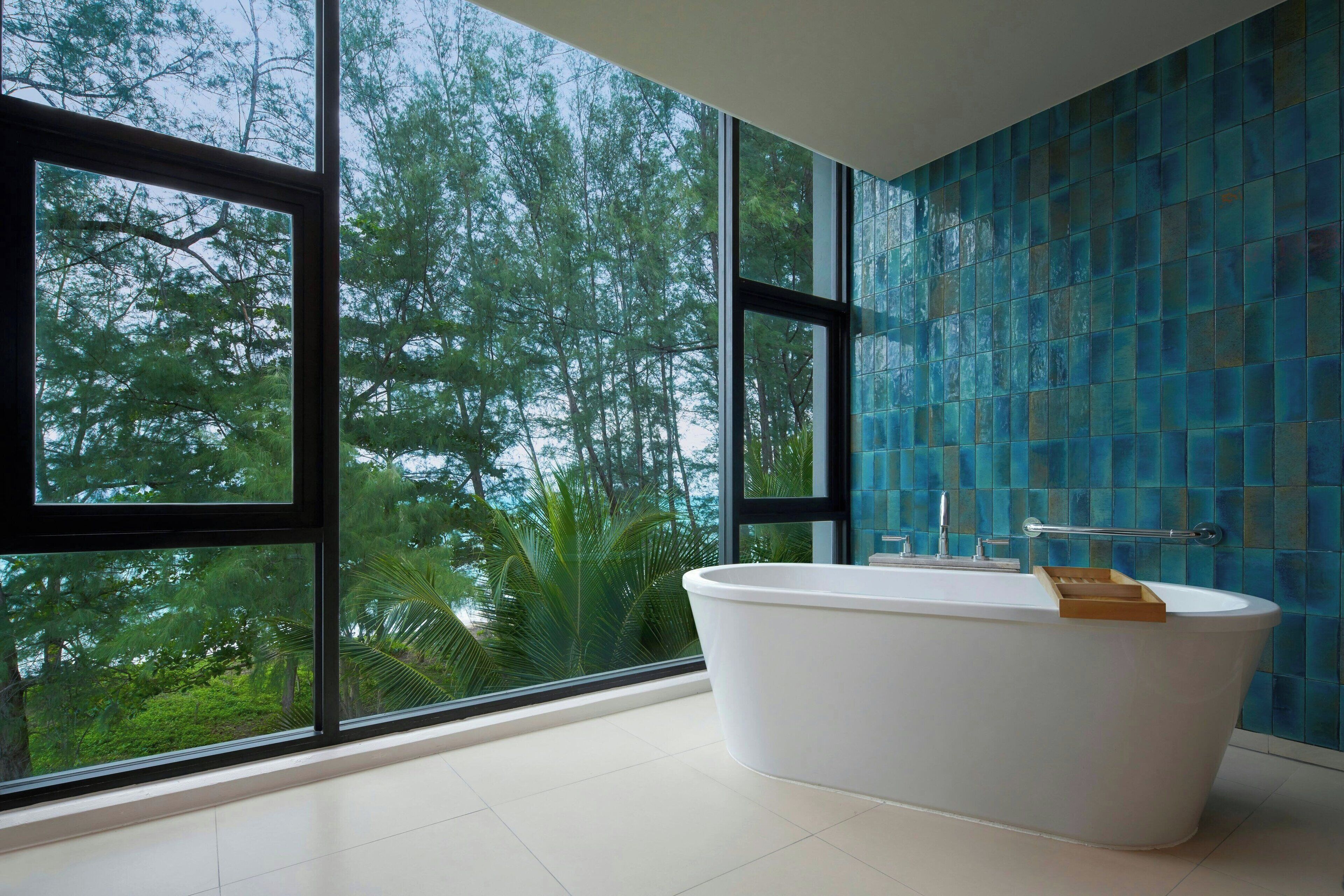 A modern bathroom with a freestanding bathtub, large windows, and a blue mosaic wall.