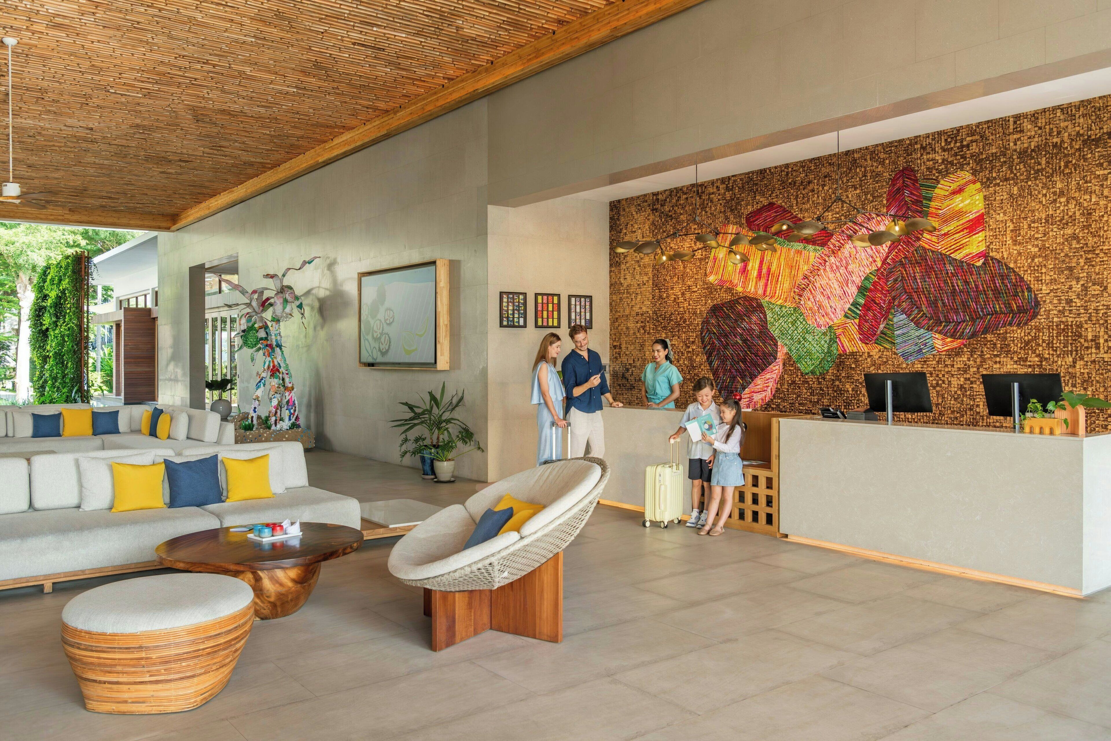 Una zona de recepción moderna con un gran mural en la pared, un mostrador de recepción y un área de estar con sofá y sillones.