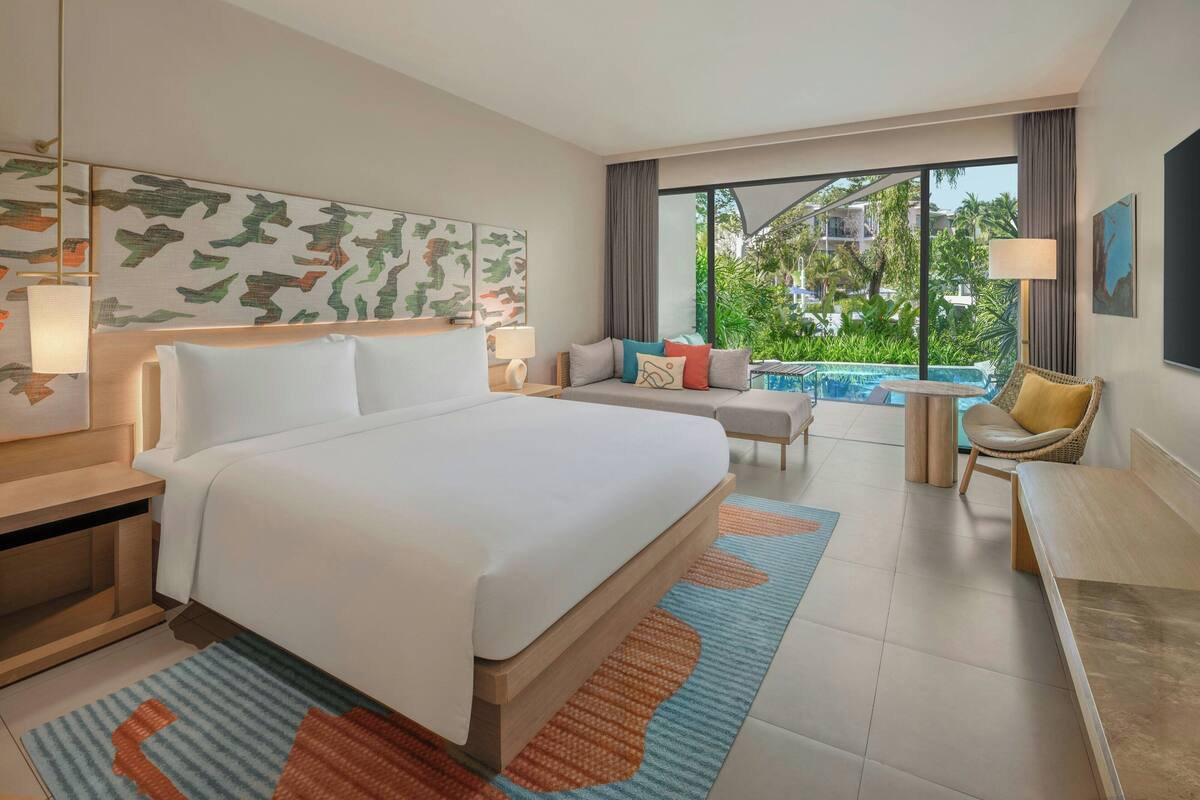 A hotel room with a large bed, a sofa, a small table, and a view of a swimming pool.
