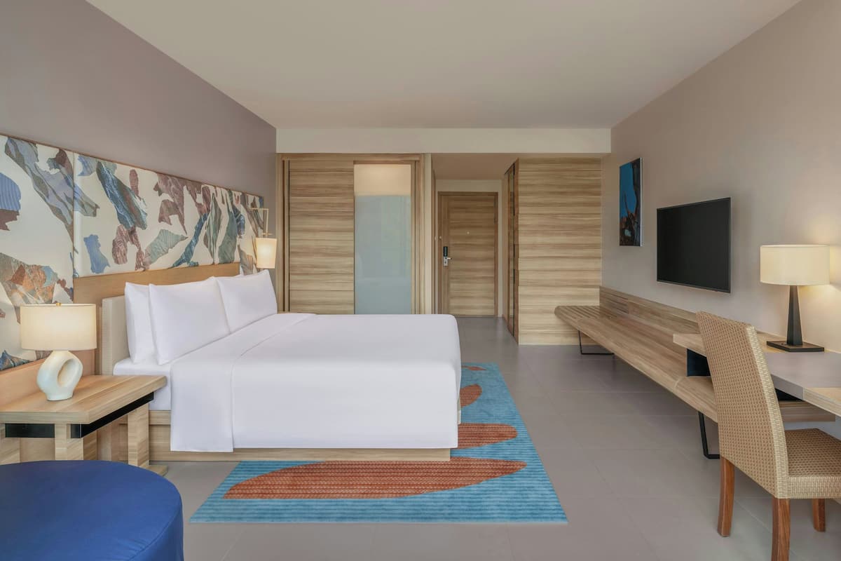 A hotel room with a bed, bedside tables, a desk, a chair, a TV, and artwork on the walls.