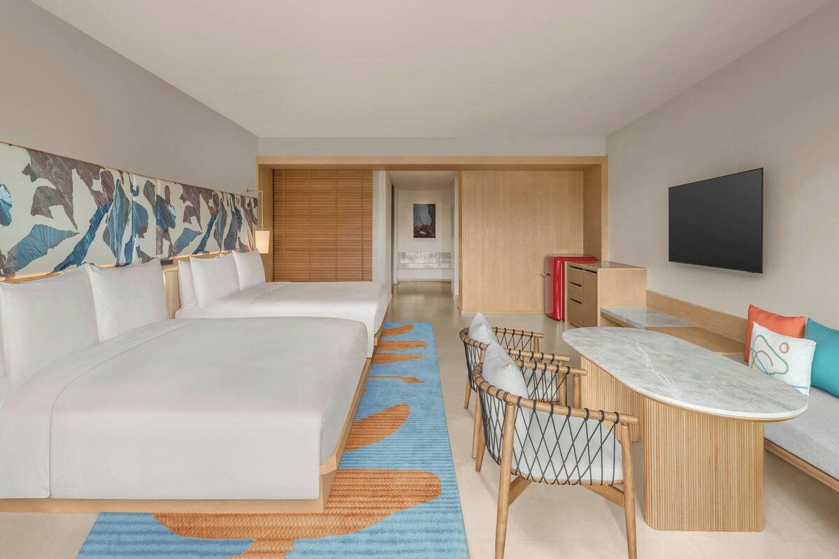 A hotel room with two beds, a dining area, a TV, and a bathroom visible through an open door.