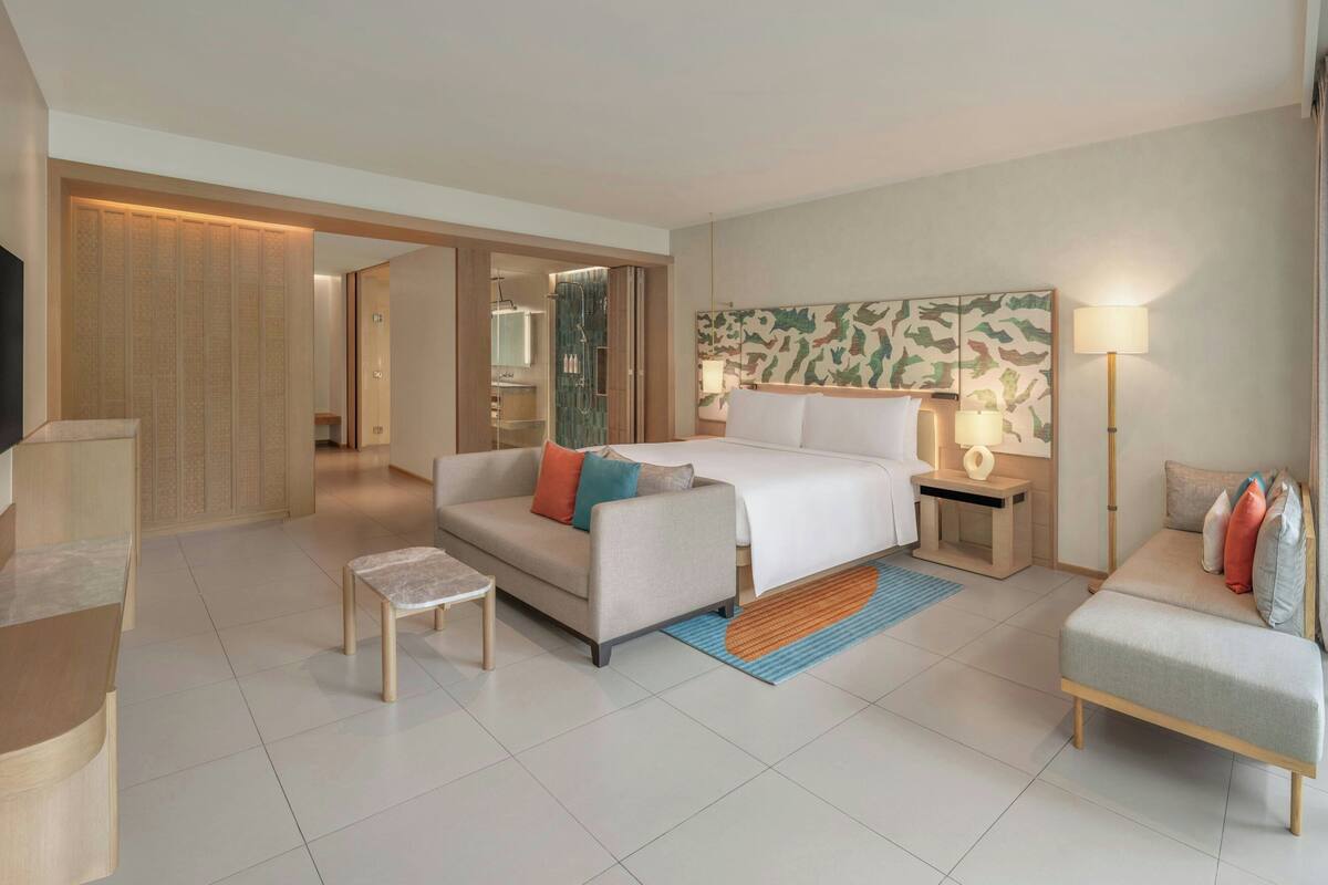 A modern hotel room with a large bed, a sofa, a small table, and a TV.