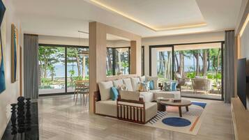 Uma sala de estar moderna com sofá, mesa de centro e televisão, grandes janelas com vista para o mar, e um espaço de jantar com cadeiras.