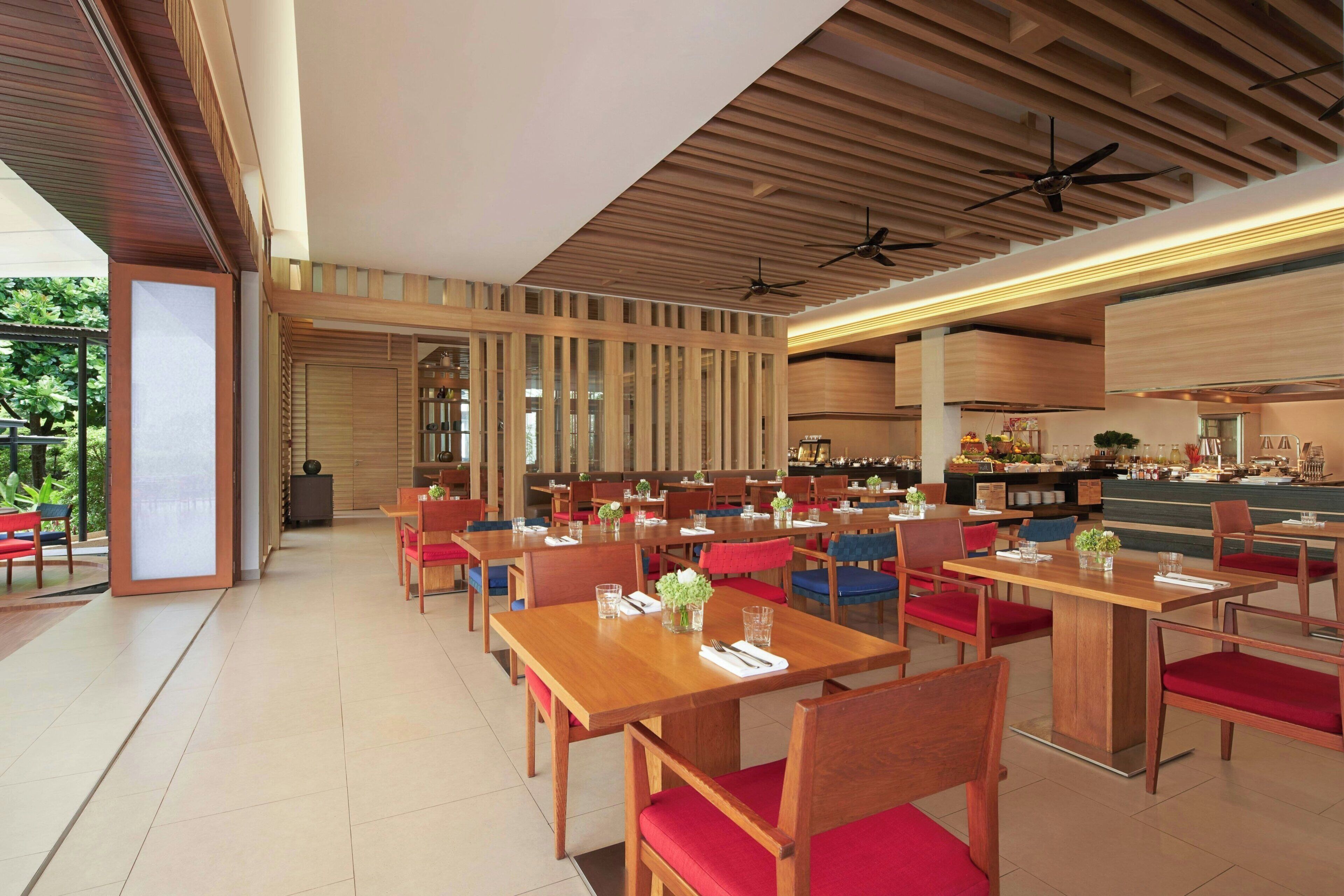Un restaurante amplio con mesas y sillas de madera, ventiladores de techo y vistas al exterior.