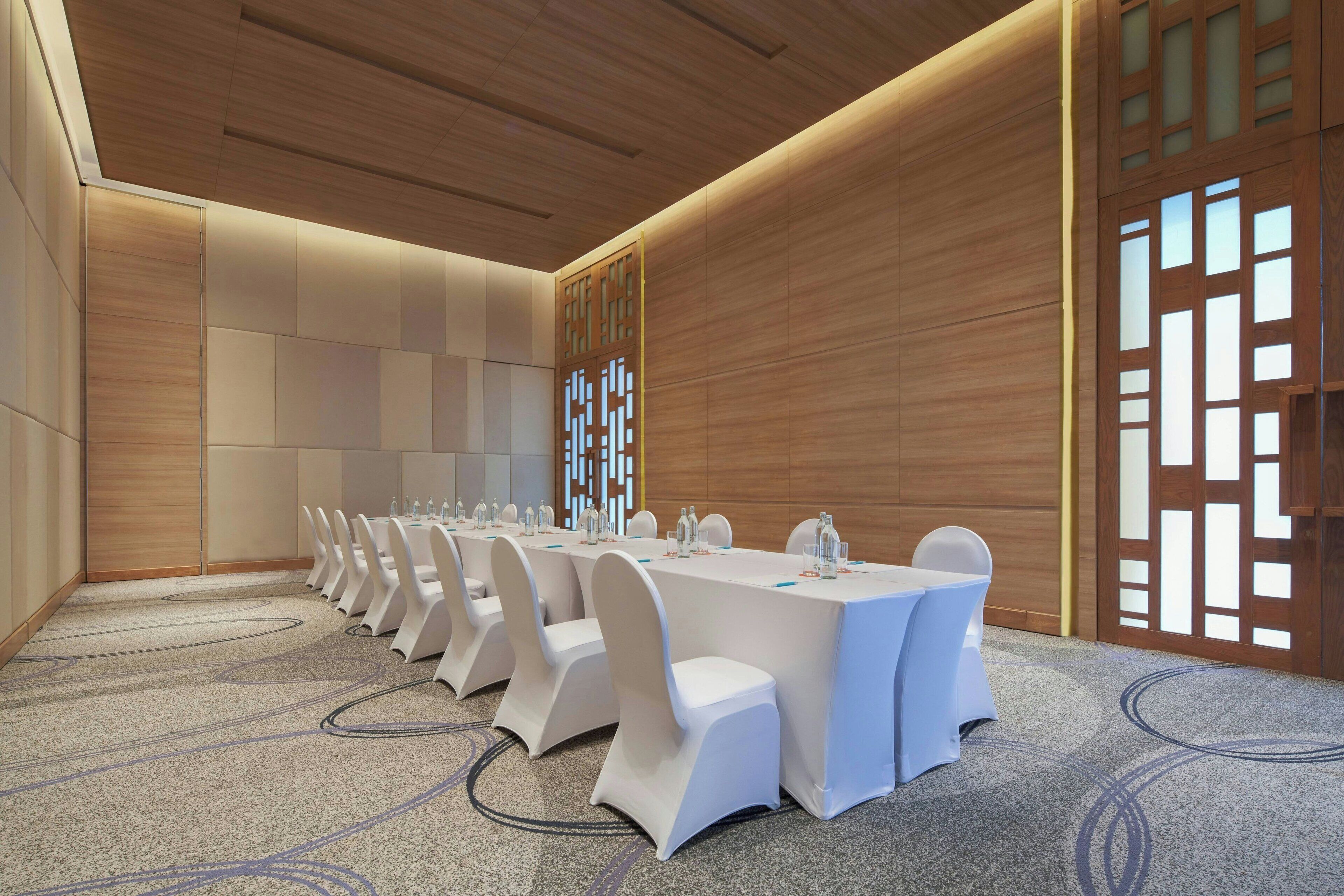 A conference room with a long table, white chairs, and a carpeted floor.