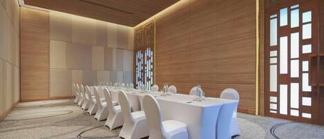 A conference room with a long table, white chairs, and a carpeted floor.