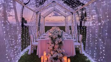 An outdoor wedding setup with a tent, white tablecloths, floral arrangements, and candles.