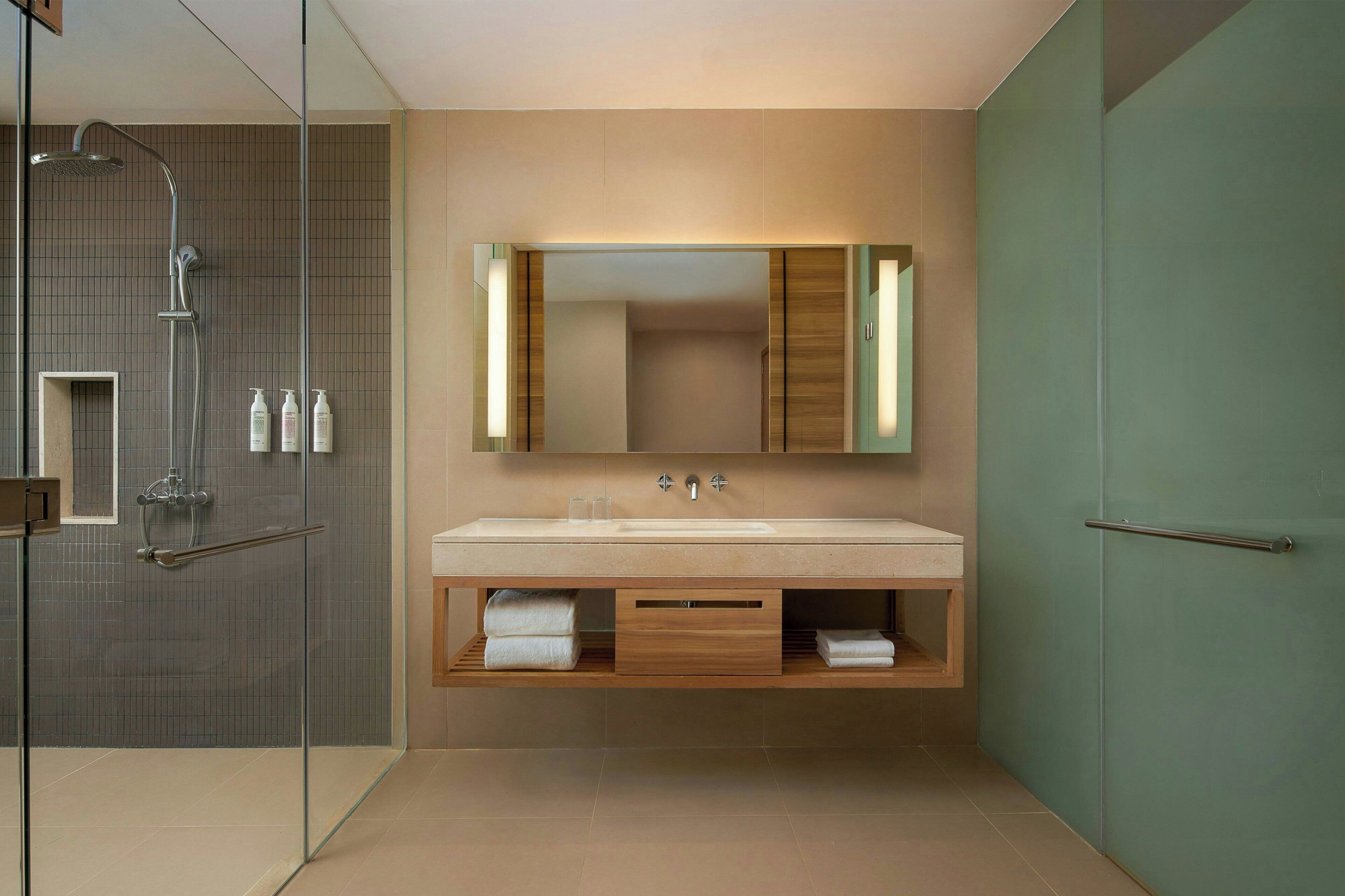 Un baño moderno con ducha envuelta en vidrio, un espejo grande y un tocador de madera con un perchero para toallas.