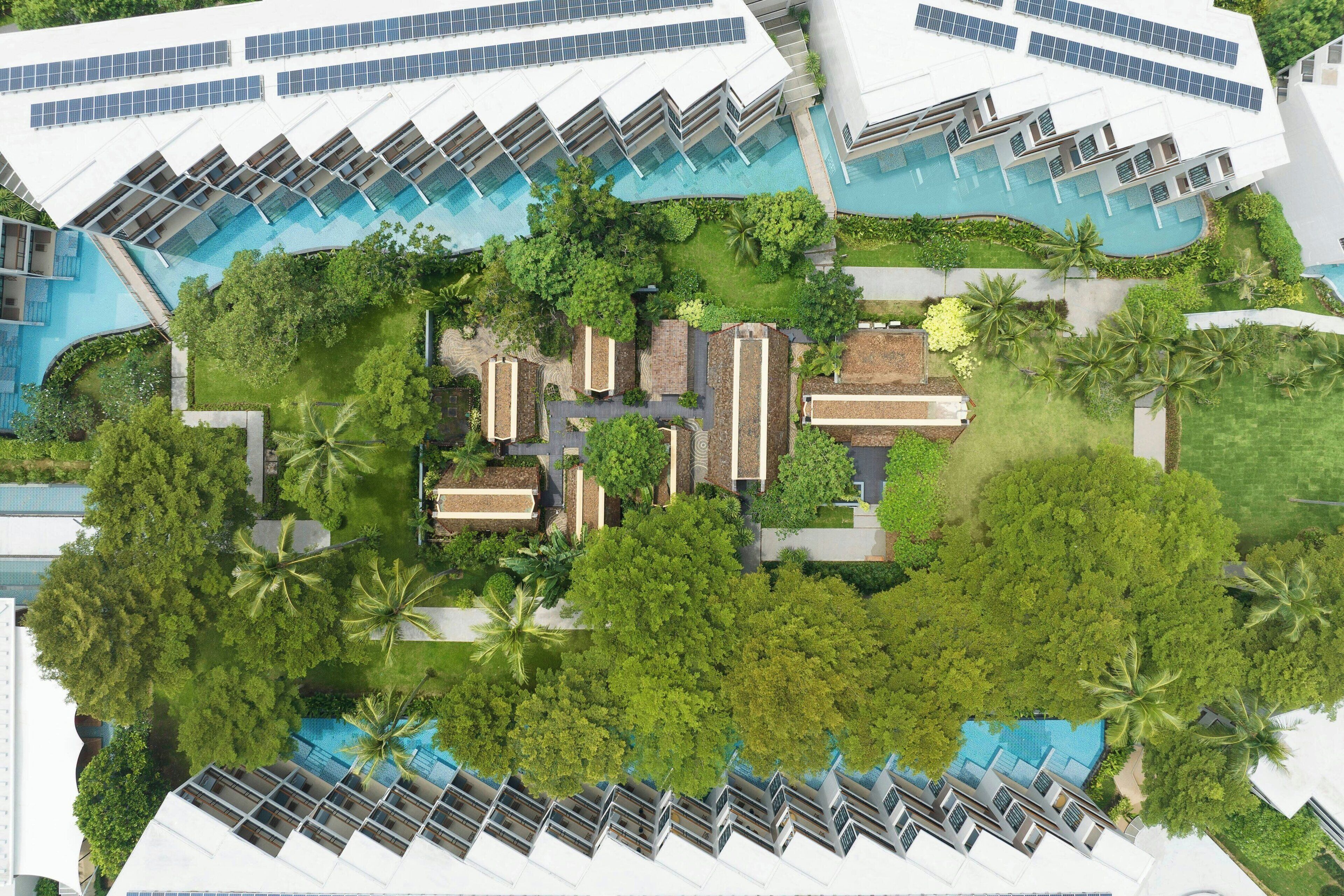 An aerial view of a hotel with multiple swimming pools, lush greenery, and modern architecture.