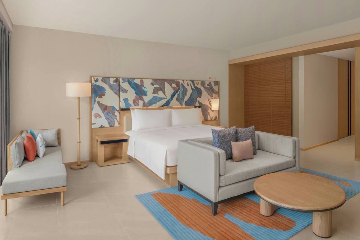 A modern hotel room with a bed, a sofa, a coffee table, and a large abstract painting on the wall.