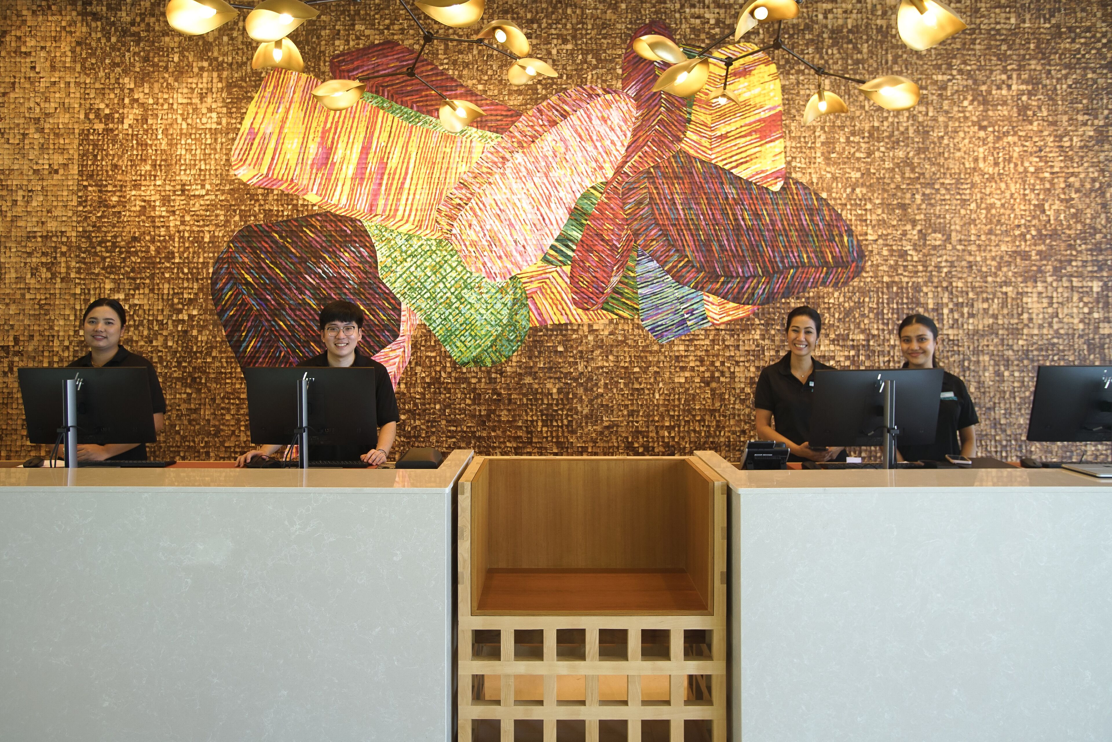 A reception desk with four staff members, a colorful abstract wall art, and a wooden panel design.