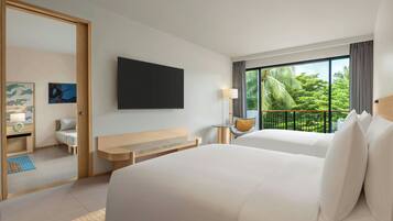 A hotel room with two beds, a desk, a chair, a TV, and a balcony with a view of greenery.