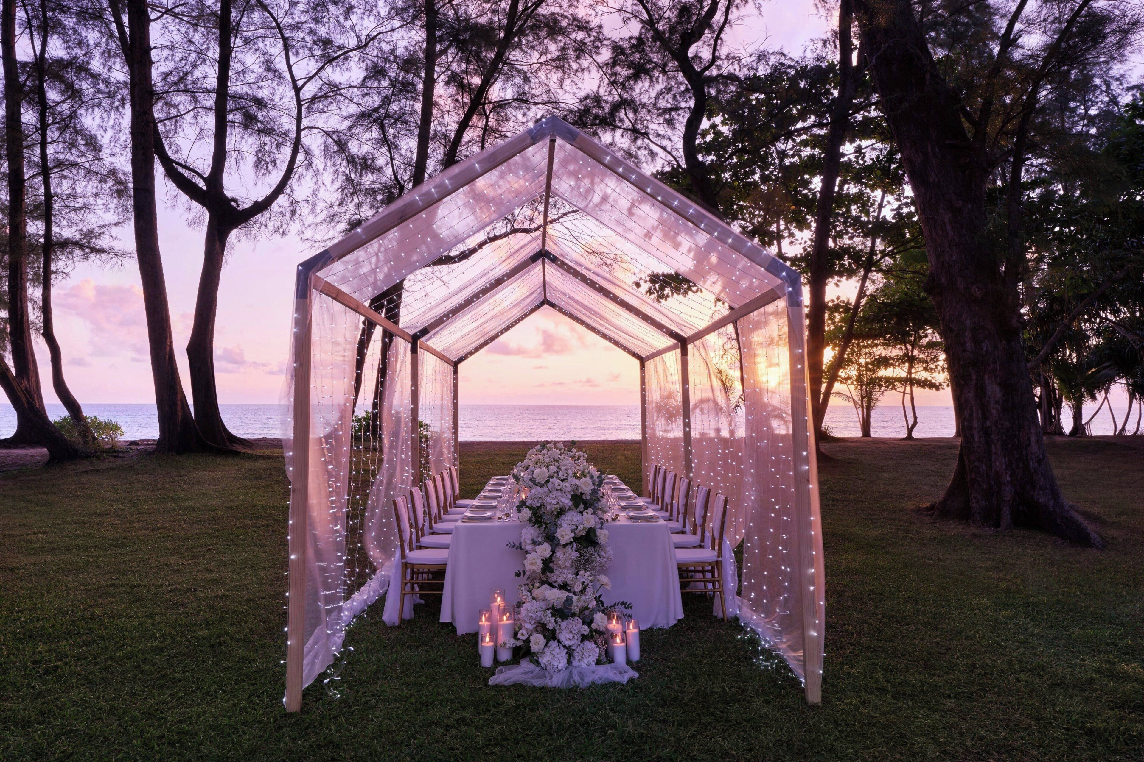 An outdoor wedding setup with a tent, tables, chairs, and floral arrangements.