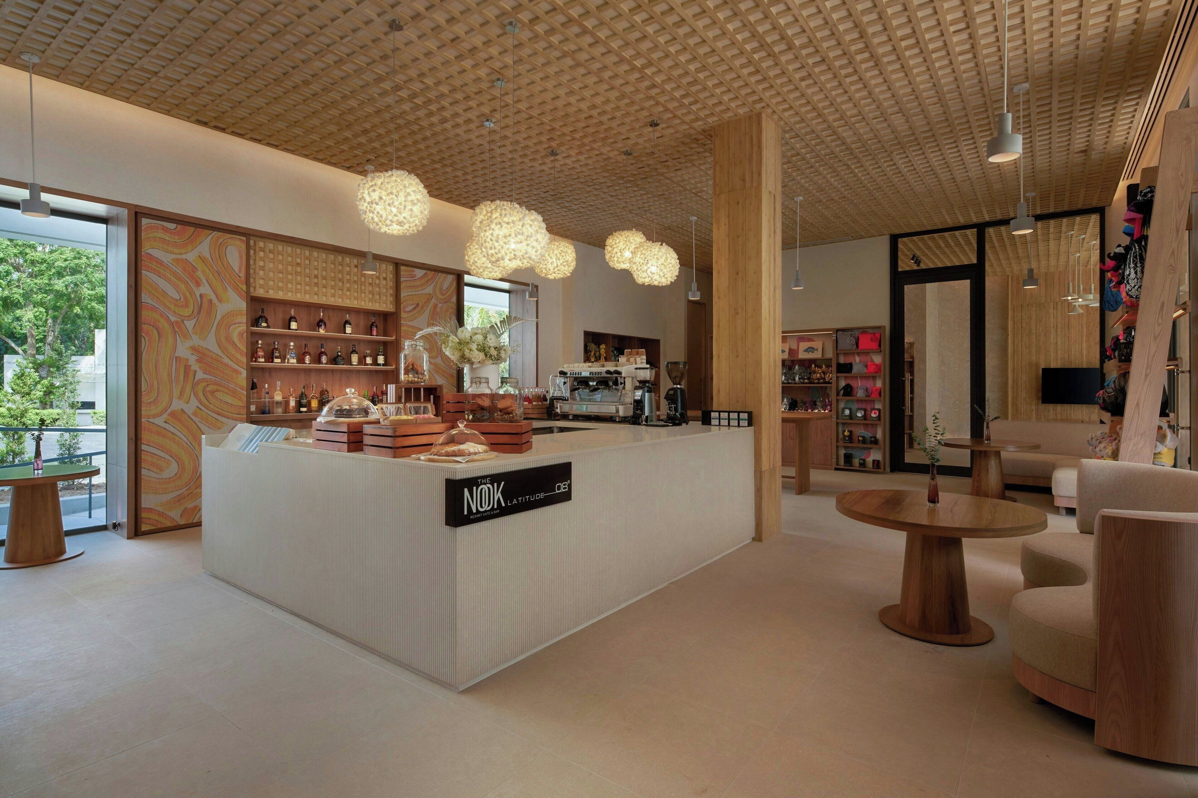 Una moderna zona de recepción con techo de madera, un mostrador central que exhibe varios artículos, y un área de descanso con mesas redondas.