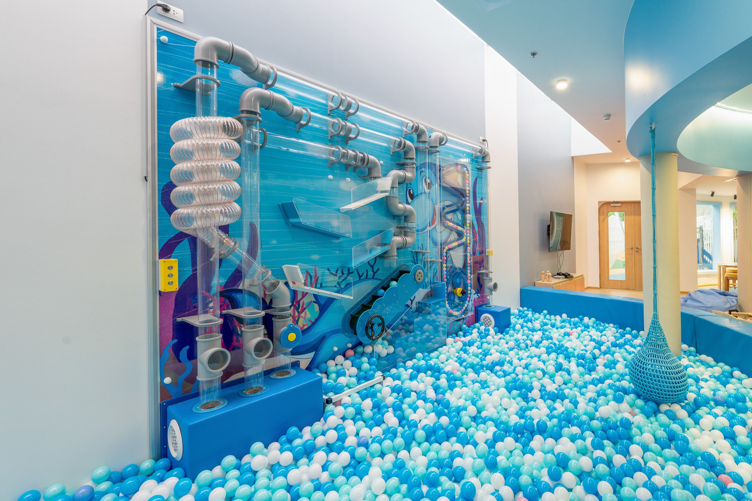 A ball pit with a large, transparent play structure filled with various tubes and pipes.