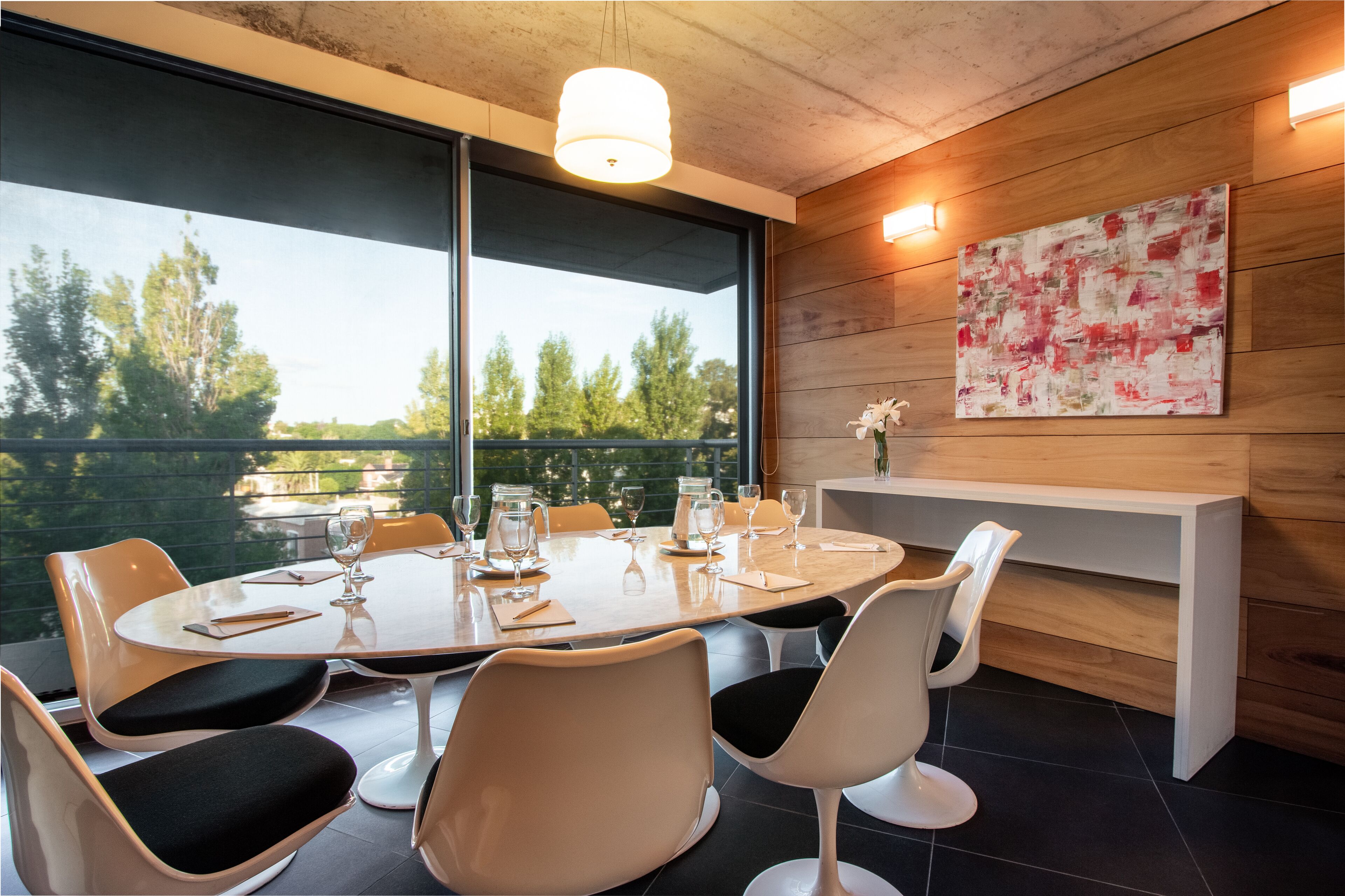 A modern dining area with a round table, white chairs, and a large window offering a view of trees.