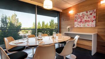 A modern dining area with a round table, white chairs, and a large window offering a view of trees.