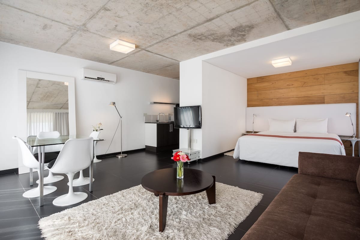 Ein modernes Hotelzimmer mit einem Bett, einem Fernseher, einem Schreibtisch mit Stühlen und einer weißen Wand.