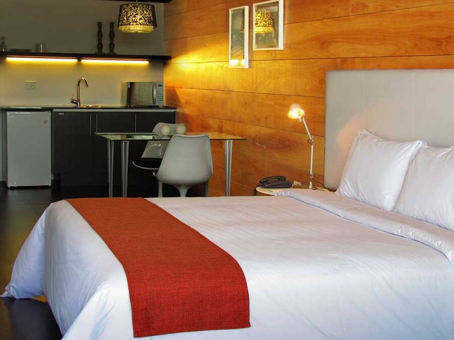 A hotel room with a bed, a desk, a chair, a lamp, and a phone.