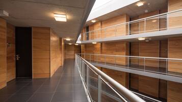 A modern interior with a long corridor, wooden panel walls, a glass railing, and a skylight.