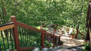 A wooden deck with a railing, surrounded by lush greenery. - Alaska Adventure Unlimited Chalets (Wasilla)