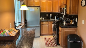 A modern kitchen with wooden cabinets, a stainless steel refrigerator, a microwave, and a coffee maker. - Alaska Adventure Unlimited Chalets (Wasilla)