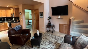 A spacious living room with a large rug, leather sofas, a flat-screen TV, and a mounted animal hide. - Alaska Adventure Unlimited Chalets (Wasilla)